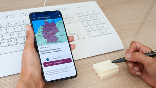 Handy vor Tastatur mit Deutschlandkarte und Warnmeldung.