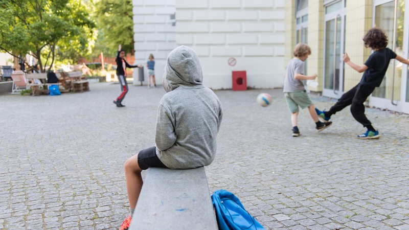 Ein Junge in einem Hoodie sitzt auf einer Hofbank