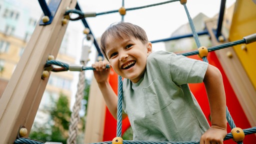 Ein lachender Junge turnt in einem Klettergerät auf einem Spielplatz