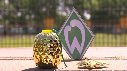 EIne goldene Ananas steht neben dem Werder Bremen Logo.