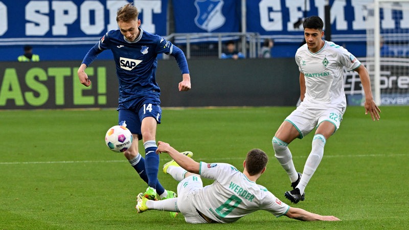 Der Hoffenheimer Maximilian Beier springt mit dem Ball über den grätschenden Werder-Spieler Mitchell Weiser.