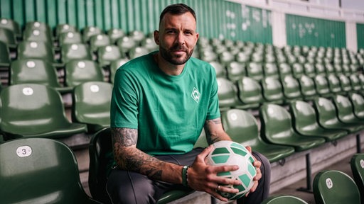 Der Werder-Torhüter Markus Kolke sitzt im Weser-Stadion auf der Tribüne und hält einen Ball in den Händen.