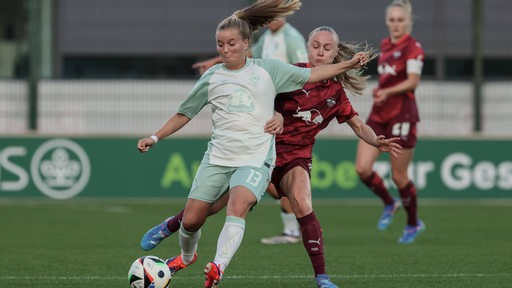 Zwei Fußballerinnen kämpfen auf dem Spielfeld um den Ball.