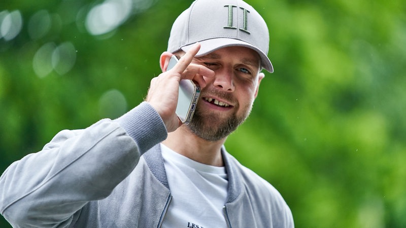 Werder-Stürmer Niclas Füllkrug in Straßenkleidung mit Handy am Ohr vor dem Weser-Stadion, grinsend, sodass seine markante Zahnlücke aufblitzt.