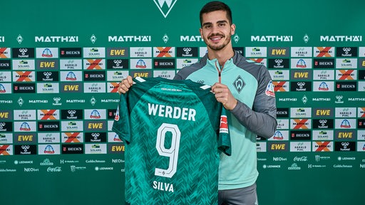 André Silva posiert mit einem Werder-Trikot in der Hand.