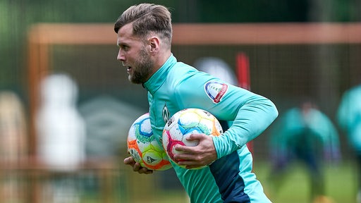 Werder-Stürmer Niclas Füllkrug rennt beim Training mit zwei Fußbällen unter beiden Armen über den Platz.