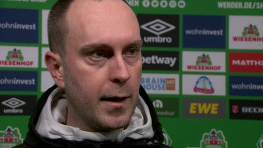 Werder-Coach Ole Werner steht vor einer Werbewand beim Interview nach dem Spiel.