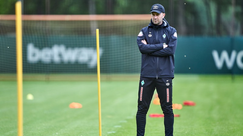 Werder-Coach Ole Werner steht mit verschränkten Armen auf dem Trainingsplatz.