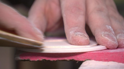 Es ist eine Hand zu sehen, welche ein Stück Holz schleift.