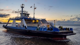 Ein Fährschiff fährt auf oin den Sonnenuntergang.