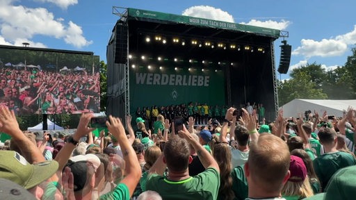 Viele Werder Bremen Fans stehen vor einer Bühne, auf welcher die Fußballspieler stehen.