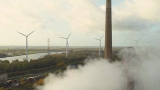 Ein Luftbild auf dem im Hintergrund Windräder zu sehen sind. Im Vordergrund aufsteigender Rauch.