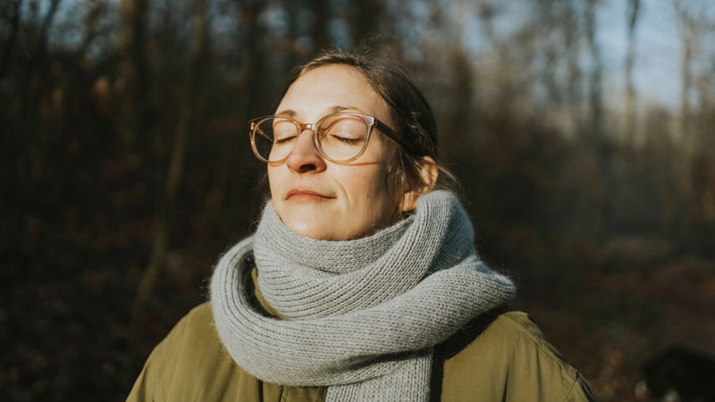 Eine Frau hält im Winter ihr Gesicht in die Sonne (Symbolbild)