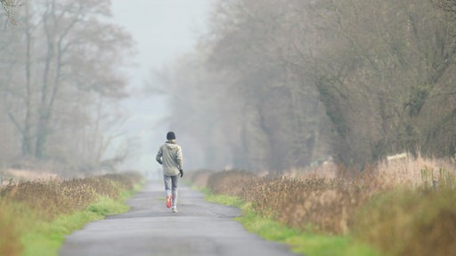 Ein Jogger läuft auf einem Feldweg bei nebligen Wetter.