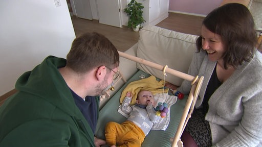 Lina und Nico Thiel knieen neben ihrer Tochter auf dem Boden.