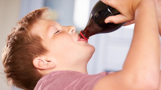 Ein Junge trinkt Cola aus einer Flasche.