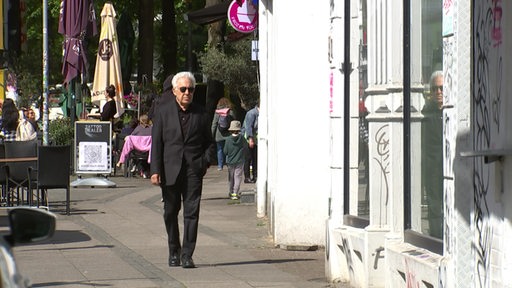 Der Musiker, Schauspieler und Filmemacher Zülfü Livaneli läuft im schwarzen Anzug mit Sonnenbrille durch das Bremer Viertel.